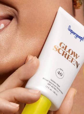 Close-up of a model holding a bottle of Supergoop! Glow Screen sunscreen