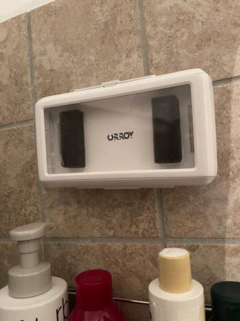 Wall-mounted soap dispenser above a row of various toiletry bottles on a tiled wall