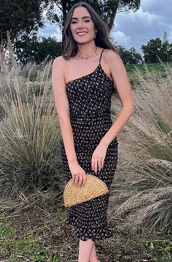 A model wearing the black floral dress with a tan bag
