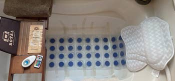 Bathtub setup with cushioned mat, remote, towel, waterproof speaker, and bath mat. Perfect for a relaxing bath experience