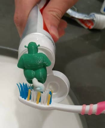 a demonstration of the topper being used as a person applies toothpaste to their toothbrush