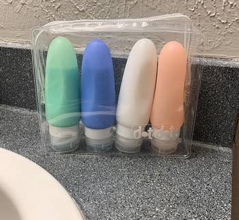 Four travel-sized toiletry bottles in a clear plastic case on a bathroom counter