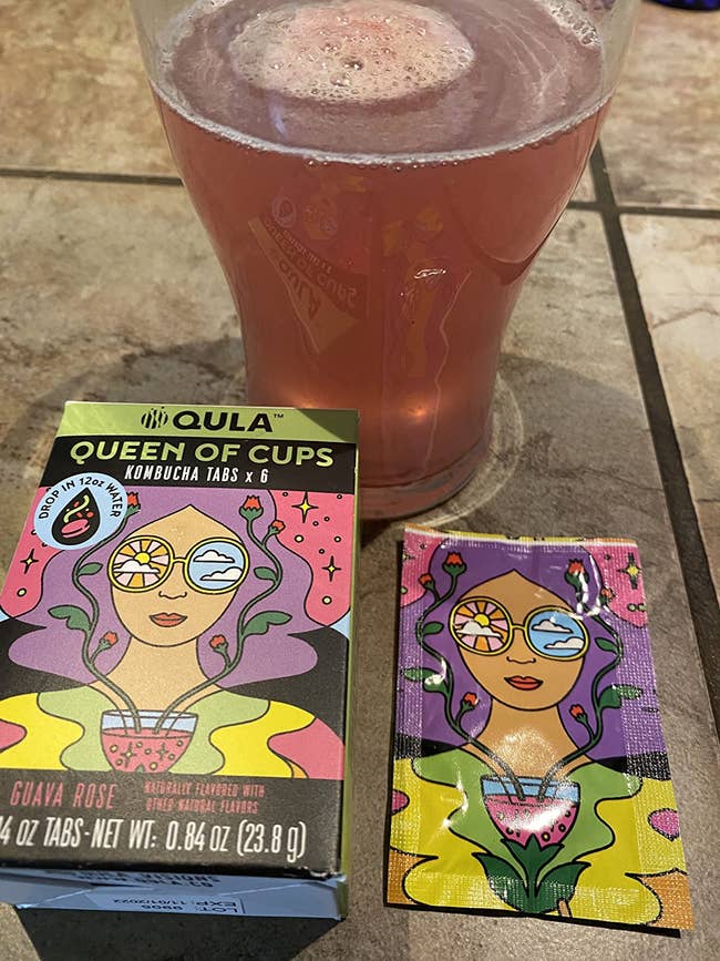 reviewer photo of their glass of guava rose kombucha and the box of kombucha tabs, which have an illustration of a woman on them