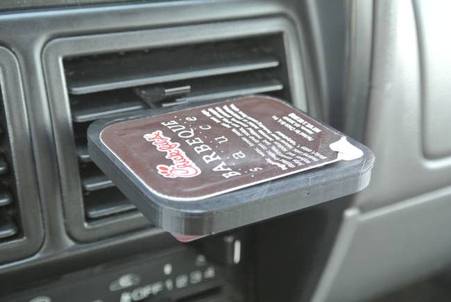 the black dip clip with one slot and barbecue sauce in it attached to the air vent in a car