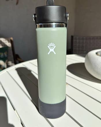 Insulated water bottle with logo on a table, sunlight highlighting its sleek design. Ideal for hydration on the go
