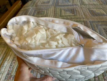 Hand holding a partially unzipped pillow showing shredded foam filling inside, highlighting its adjustable comfortableness  feature