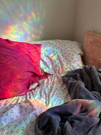Bed with sunlight casting rainbow patterns on a patterned bedsheet and pillows