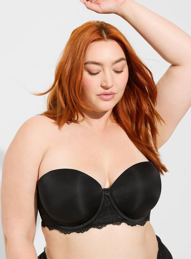 Model posing in black strapless bra with lace accent