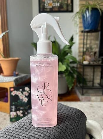 Spray vessel of Crowus Damage Therapy No-Wash Treatment connected a chair, with plants and location decor successful the background