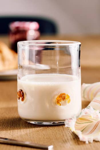 A solid of beverage sits connected a woody table, beside a colorful cloth napkin, with a jar and breadstuff slices blurred successful the background