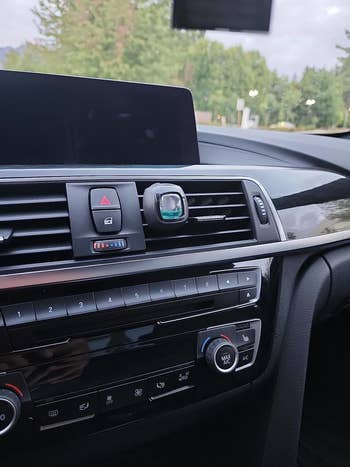 Car interior showing dashboard controls, an air vent with a green air freshener attached