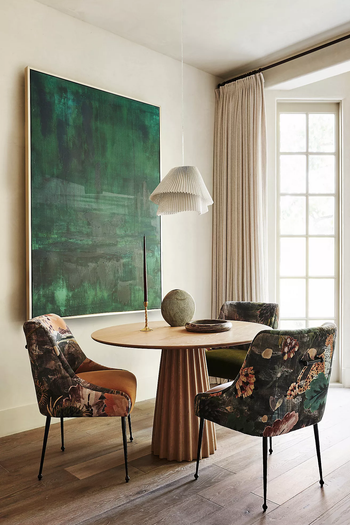 Elegant dining area with a round table, four floral upholstered chairs, a large abstract green artwork, and a hanging lamp