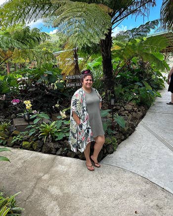 Woman in a casual dress with a floral cover up standing in a garden pathway
