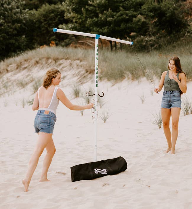 Two models on a sandy beach, playing with a portable swingball set