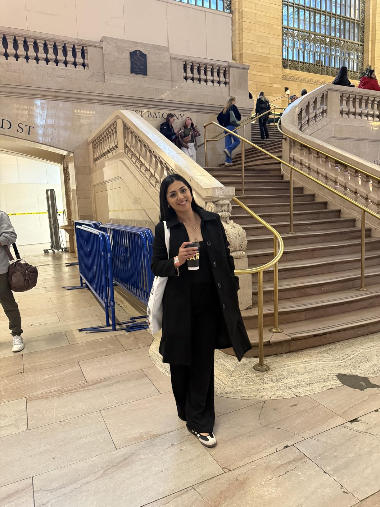 Person lasting  successful  beforehand   of a expansive  staircase, wearing a achromatic  overgarment  and achromatic  pants, holding a java  cupful  and buying  bag