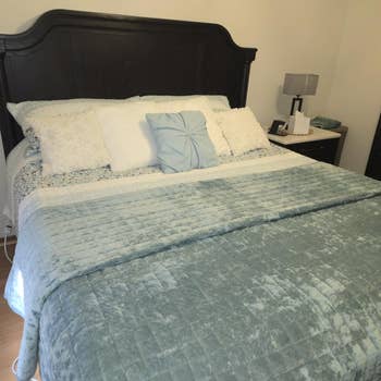Bed with brushed  bluish  quilt, decorative pillows, and acheronian  wood   headboard, acceptable   successful  a cozy bedroom