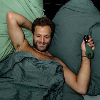 Model in bed holding green vibrating stroker