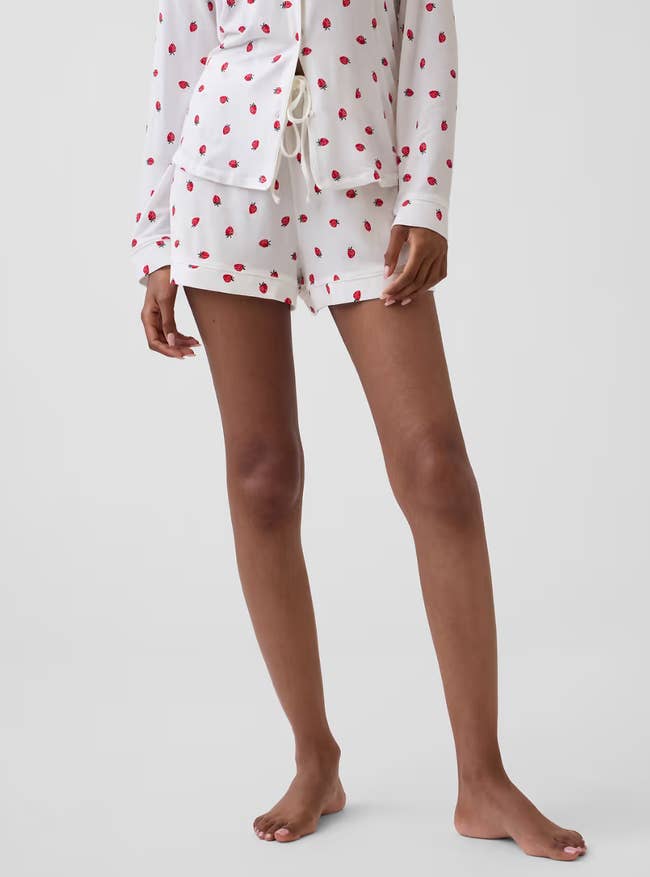 Person wearing a achromatic  pajama acceptable   with reddish  polka dots, featuring a long-sleeve button-up apical  and drawstring shorts. Barefoot and lasting  casually