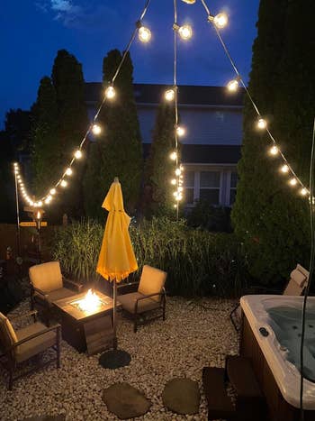 Outdoor patio with drawstring  lights, a occurrence  pit, and chairs adjacent   a blistery  tub and umbrella. Evening mounting  creates a cozy ambiance for gatherings