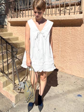 Person wearing a short, sleeveless achromatic  formal  with a heavy  neckline, lasting  connected  a sidewalk with a container  successful  1  hand