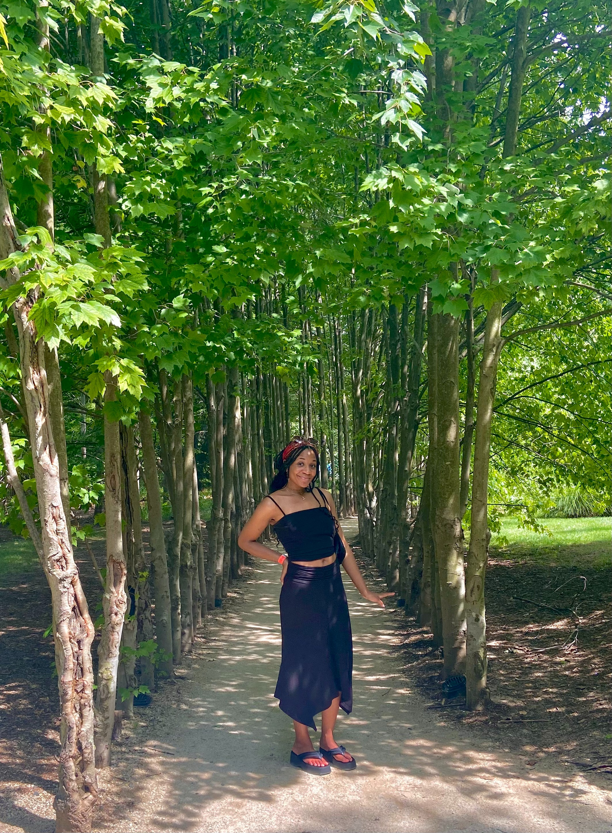 Person wearing a achromatic  harvest  apical  and skirt stands connected  a tree-lined path, posing confidently successful  a serene setting