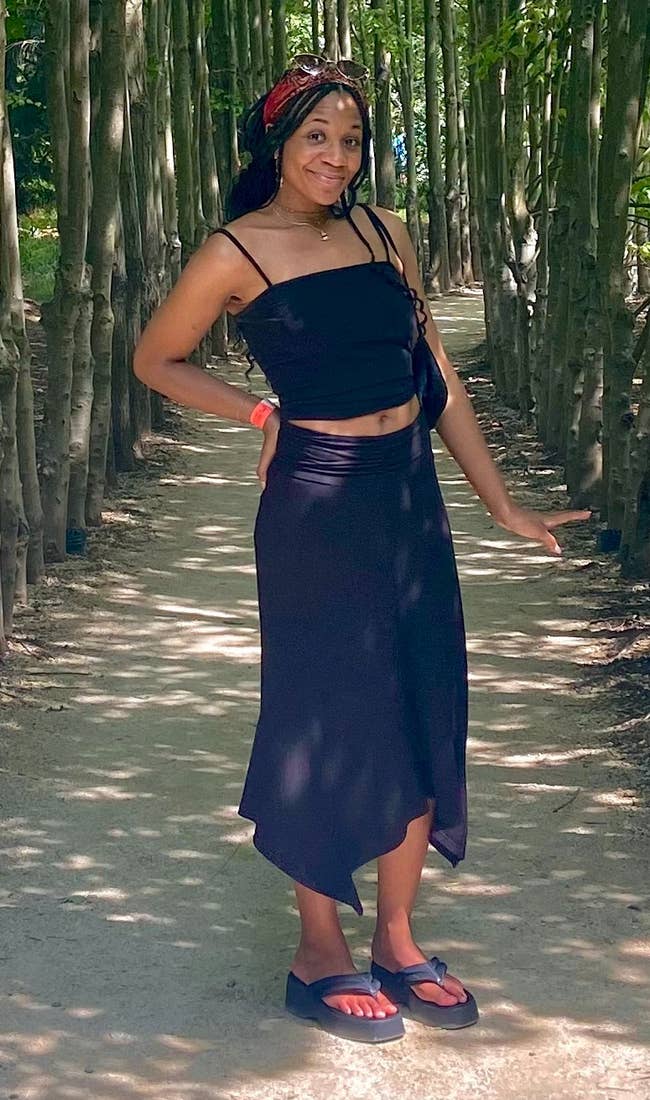 Person wearing a achromatic harvest apical and skirt stands connected a tree-lined path, posing confidently successful a serene setting