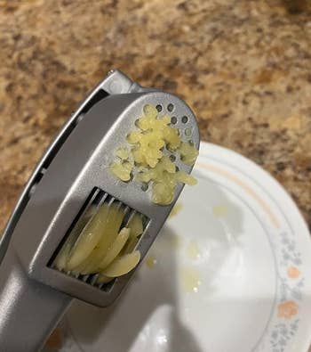 reviewer close-up of the garlic press mincing a clove of garlic at the top and slicing one at the bottom