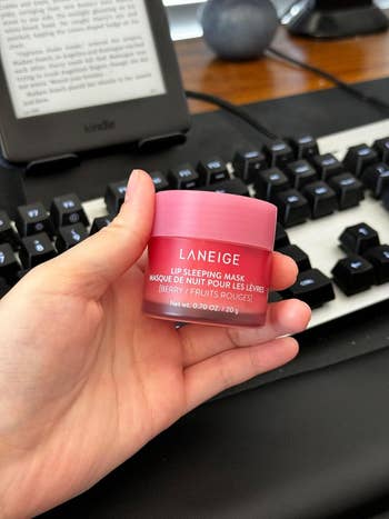 A hand holds a jar of Laneige Lip Sleeping Mask (Berry), with a keyboard and e-reader in the background