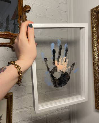 Person holds a framed handprint artwork with a shadow box effect