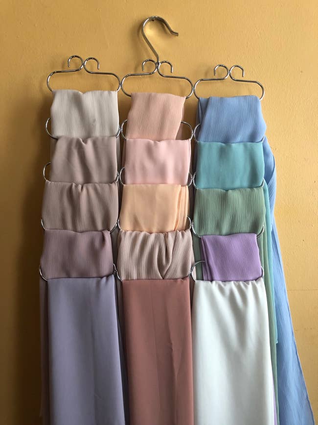 Scarves in various soft shades hang on a multi-tier hanger against a wall, showcasing a stylish and organized display for accessory storage