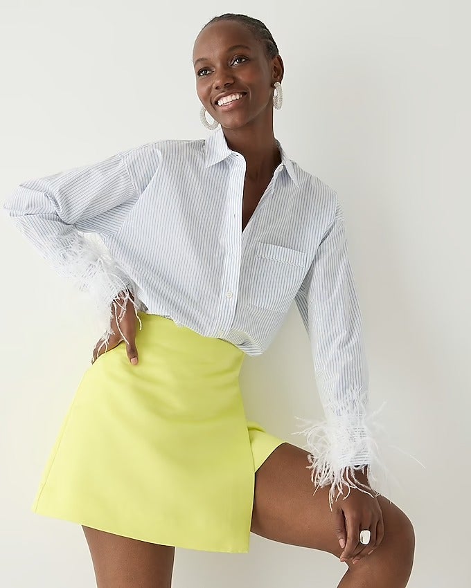 model wearing the white striped button down shirt with white feathers on the sleeve cuffs