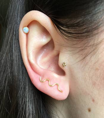 Person's ear with three earrings: a stud, a small hoop, and a squiggle-shaped earring
