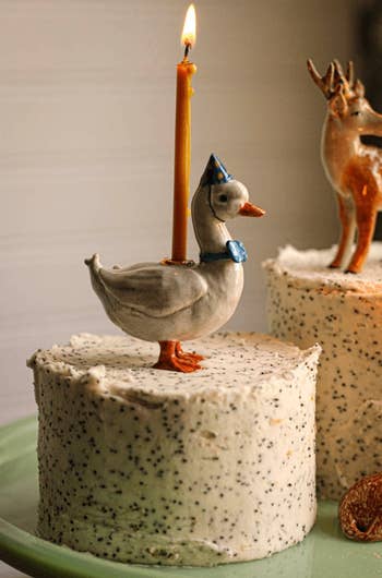 a ceramic goose atop a cake holding a lit candle