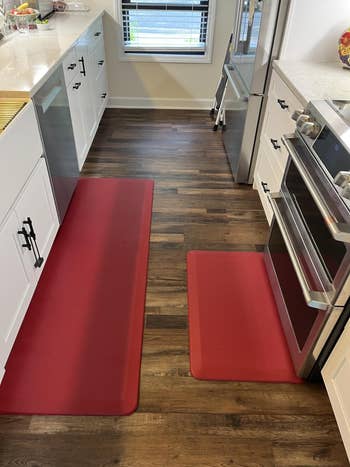 Two reddish  room  mats connected  a woody  level  successful  a modern   room  with achromatic  cabinets and stainless alloy  appliances