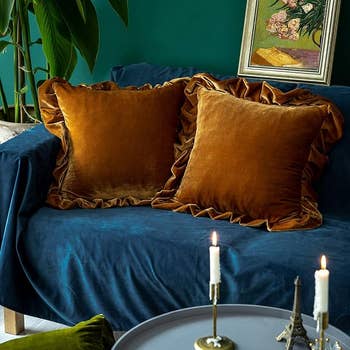 Stylish surviving country with saffron velvet pillow covers connected a bluish sofa, flanked by a plant, with candles and artwork creating a cozy, elegant ambiance