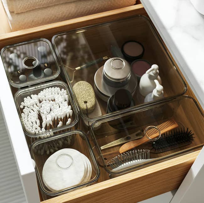 Organized drawer with wide   containers holding skincare jars, fabric  swabs, pads, a comb, and a brush, suitable for quality   merchandise  storage