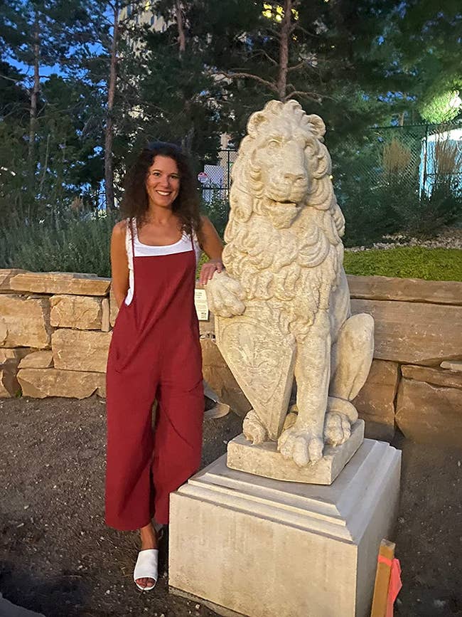 Reviewer wearing red overalls with white shirt, standing next to lion statue