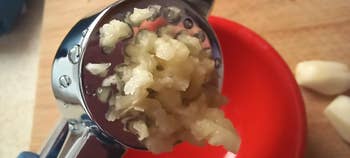 Close-up of ail  being pressed done  a ail  property   implicit    a reddish  plate, with full   ail  cloves adjacent    connected  a woody  surface