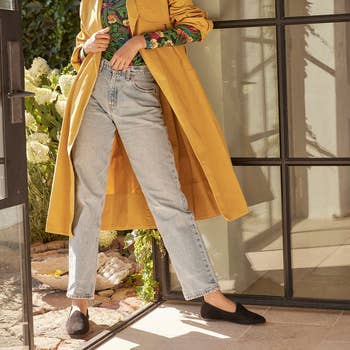 Model standing in a doorway wearing a yellow jacket and pair of jeans with the black, suede, round toe shoes