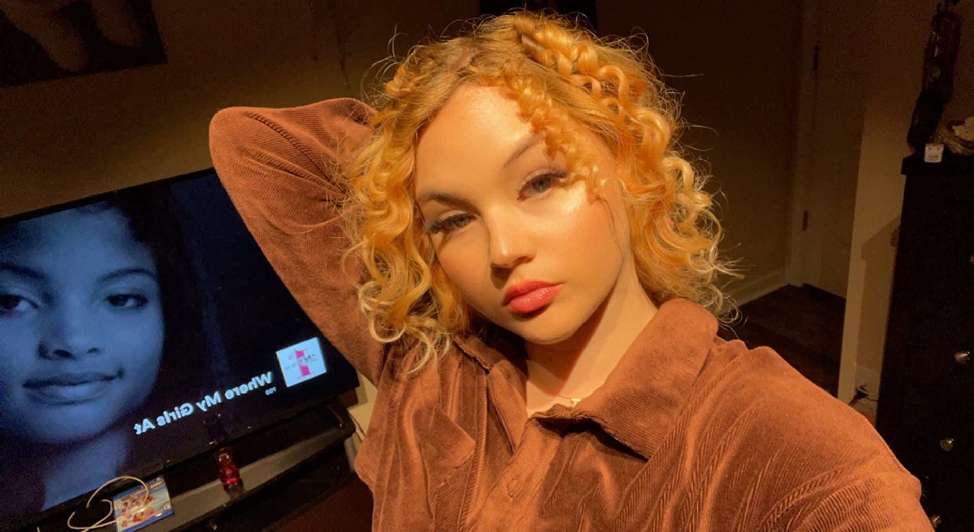 Person with curly hairsbreadth  poses successful  a stylish velvety blouse wrong  a room. A TV successful  the inheritance  displays a black-and-white face