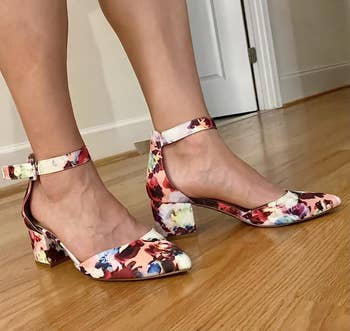 Person wearing floral-patterned block-heeled shoes with ankle straps connected a woody floor