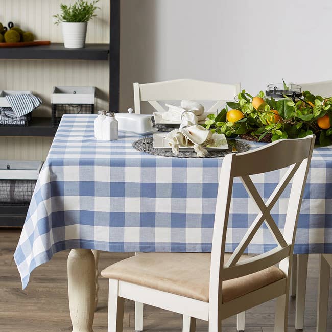 Checkered tablecloth on dining table with lemons and plants. White chairs and shelves in the background create a cozy dining area