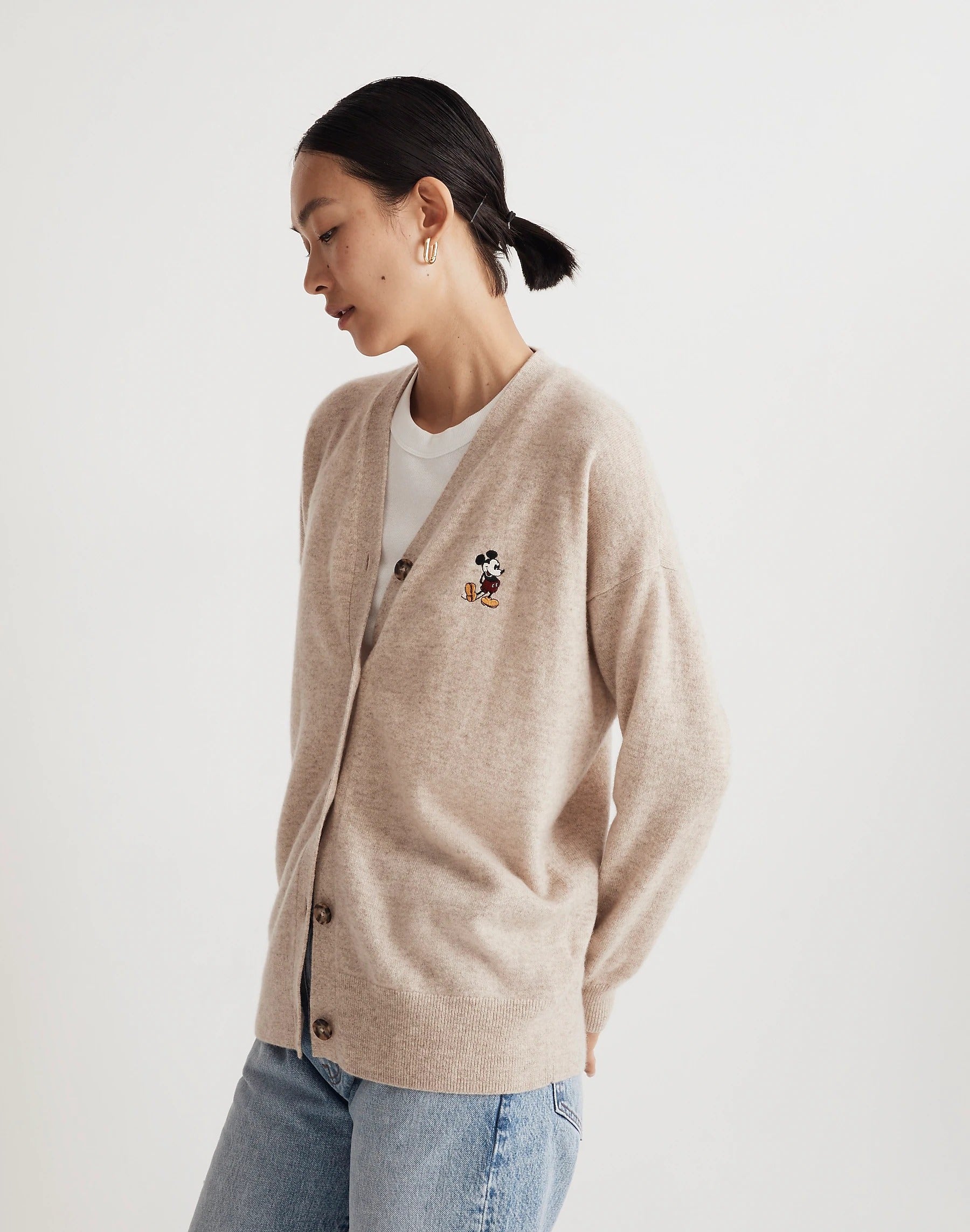 a model in a tan cardigan with a tiny mickey mouse embroidered on it