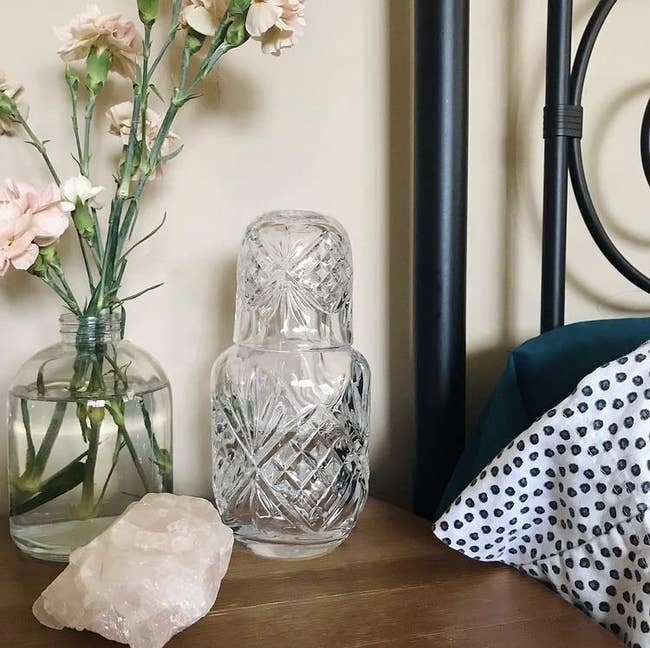 Crystal h2o carafe acceptable connected a bedside array with caller flowers successful a vase, a crystal, and a textured pillow