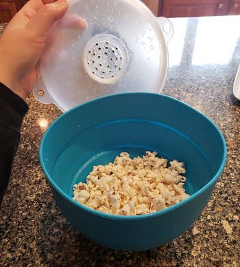 reviewer holding open the teal silicone popper with popcorn inside it