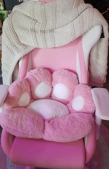 reviewer photo of a pink cat paw cushion with white pads on a pink gaming chair