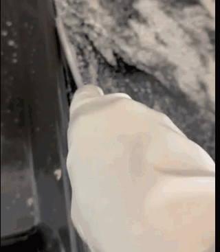 Hand in a glove spreading dough on a surface, showing a close-up of a baking process