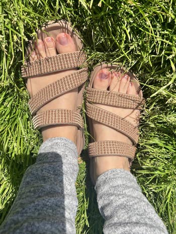 Person wearing rhinestone-studded sandals and grey leggings lasting connected grass