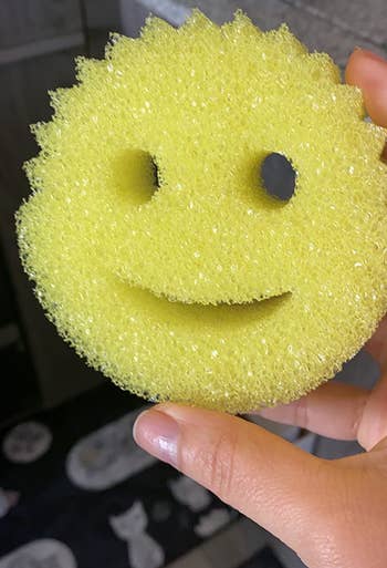 reviewer's hand holding the yellow scrub daddy, which has a smiley face design