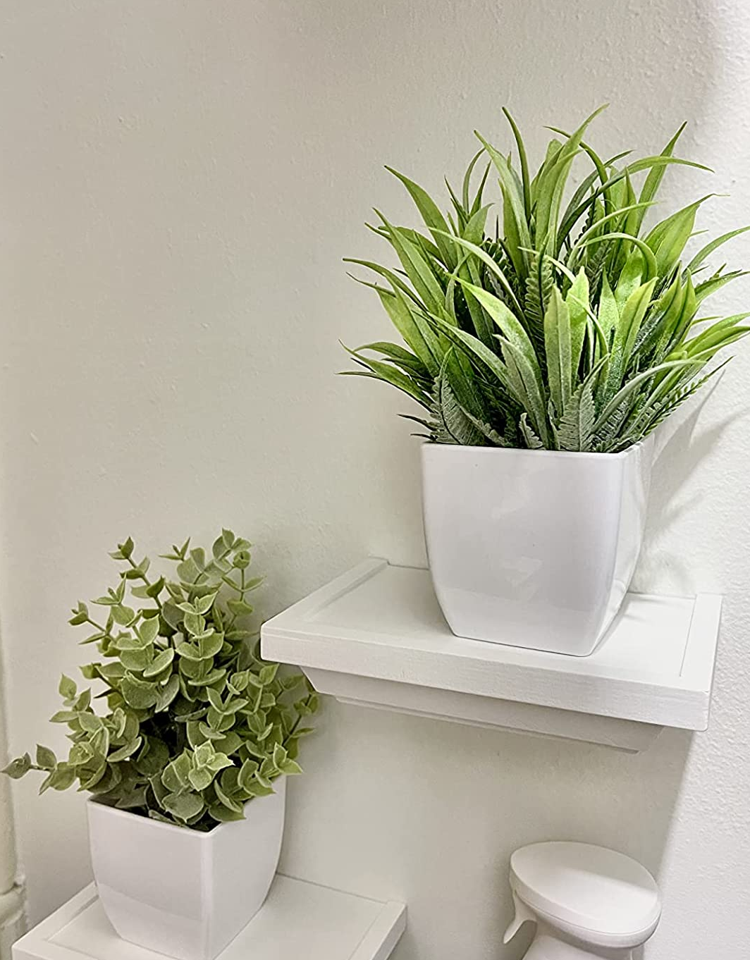 Reviewer image of two small fake plants in white pots on top of small white floating shelves on a white wall